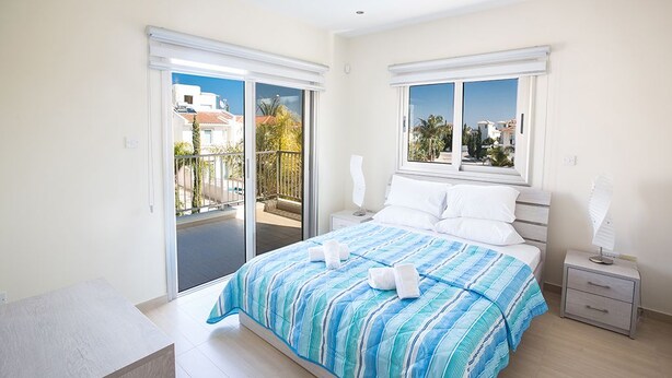 A bedroom with a bed, a nightstand, a window, and a balcony. - Protaras Villa Theodora 1 - CHG (Paralimni)