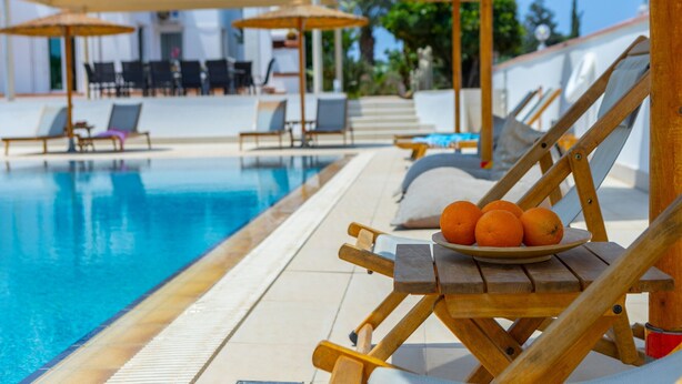 A poolside area with lounge chairs, umbrellas, and a plate of oranges.