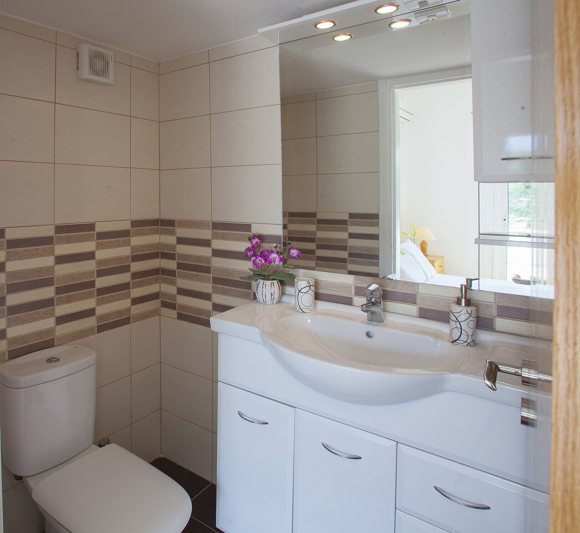 Une salle de bain équipée de toilettes, d’un lavabo, d’un miroir et de carreaux décoratifs.