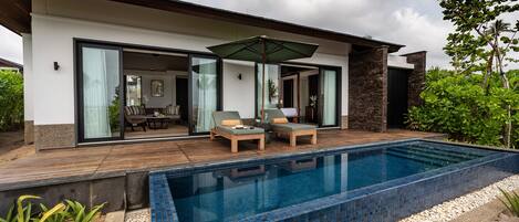 A modern house with a swimming pool, two lounge chairs, and a patio area.