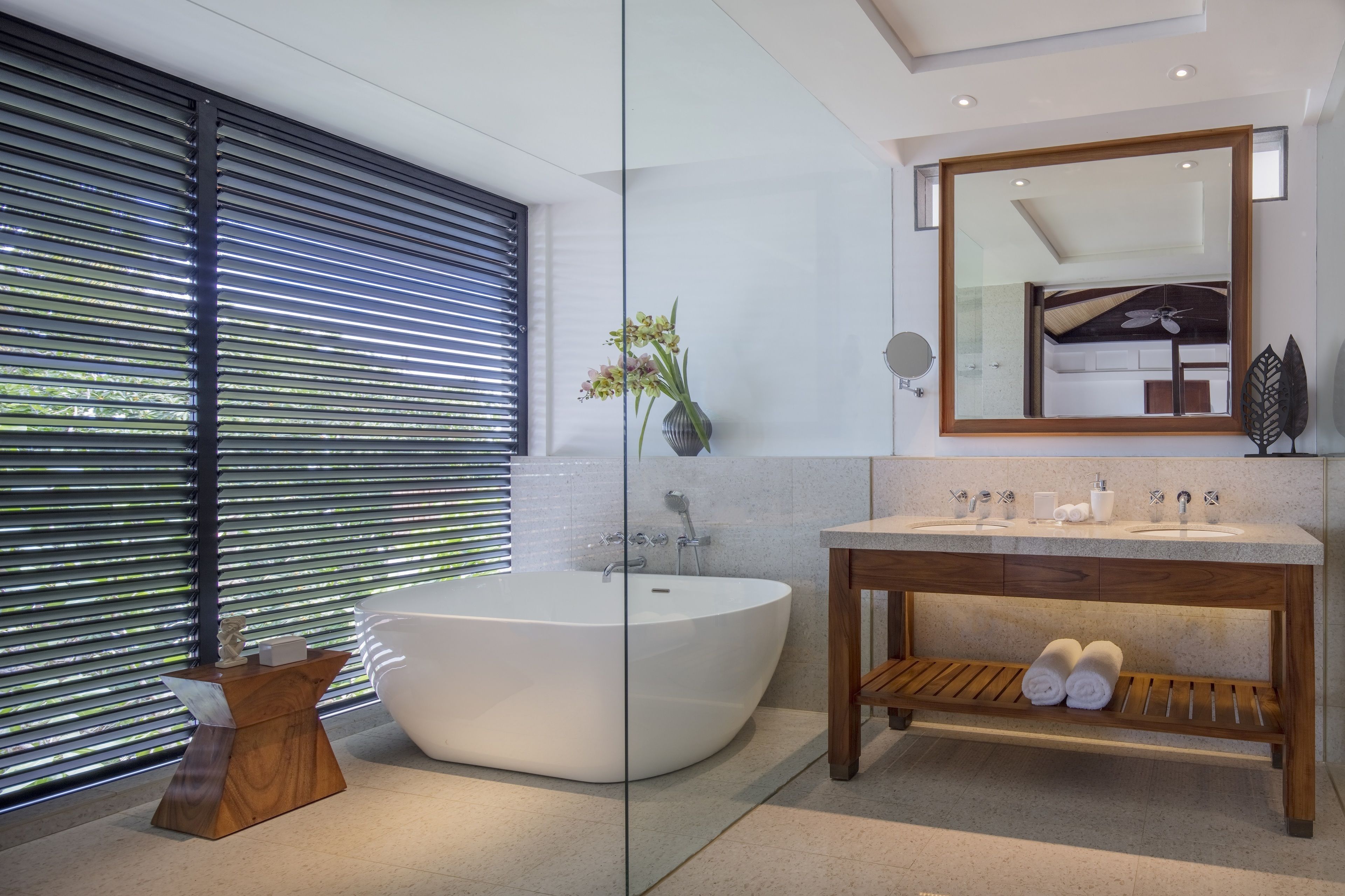 Un baño moderno con una bañera independiente, un tocador de madera y un espejo grande.