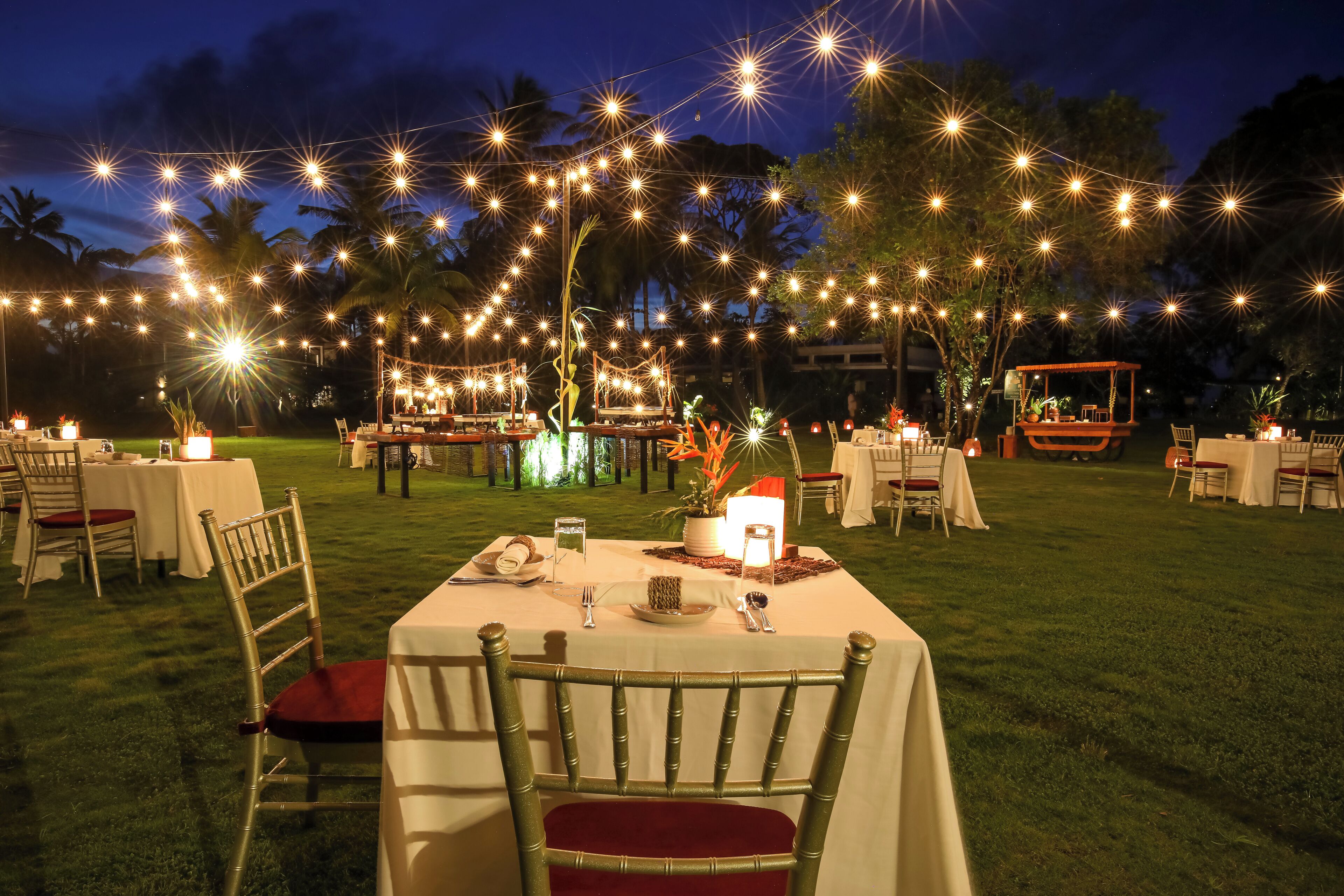 An outdoor dining area with string lights, tables, chairs, and a decorative cart.