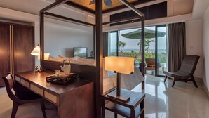 A hotel room with a wooden desk, a chair, a bed with a canopy, a TV, and a balcony with a view of the ocean. - The Residence Bintan (Bintan)