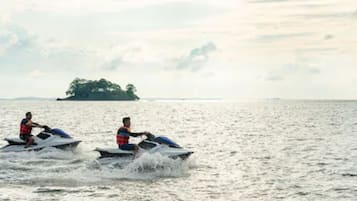 Two people jet-skiing on a body of water with a distant island.