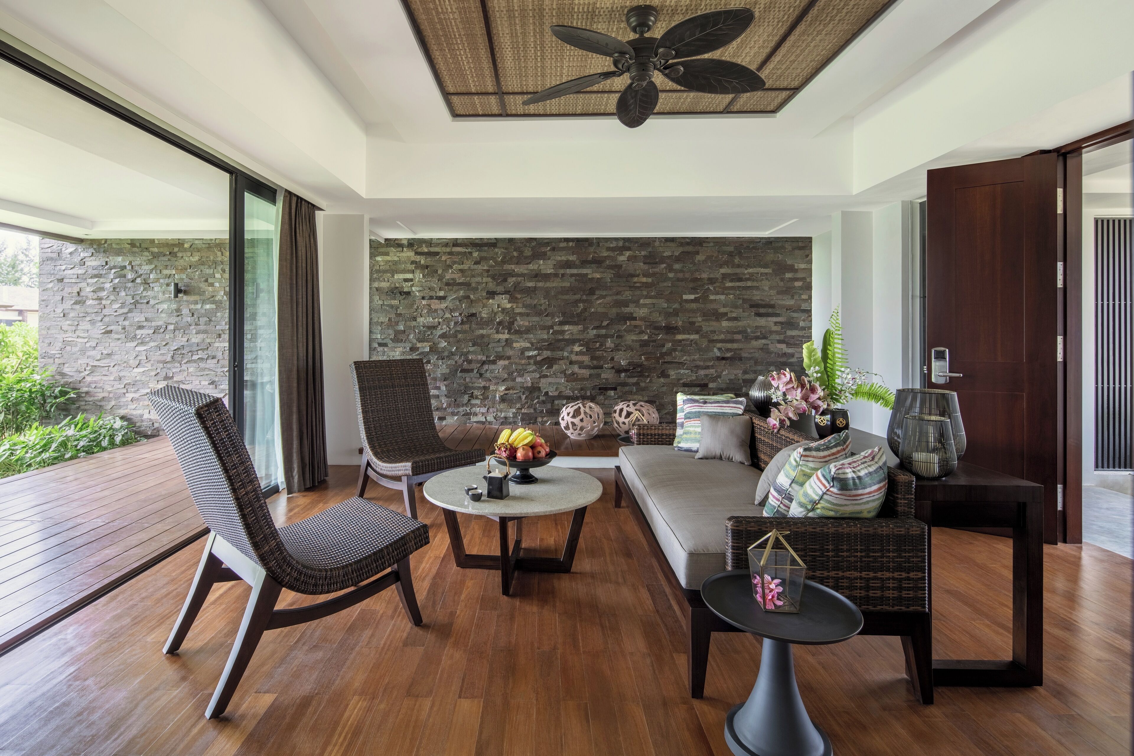 A modern living room with a stone wall, a ceiling fan, and a wooden deck.