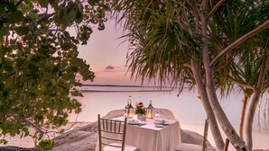 A table set for two with a view of the ocean, surrounded by palm trees and rocks. - The Residence Bintan (Bintan)