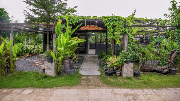 A garden entrance with a wooden sign reading "Earth Basket," surrounded by lush greenery and potted plants. - The Residence Bintan (Bintan)