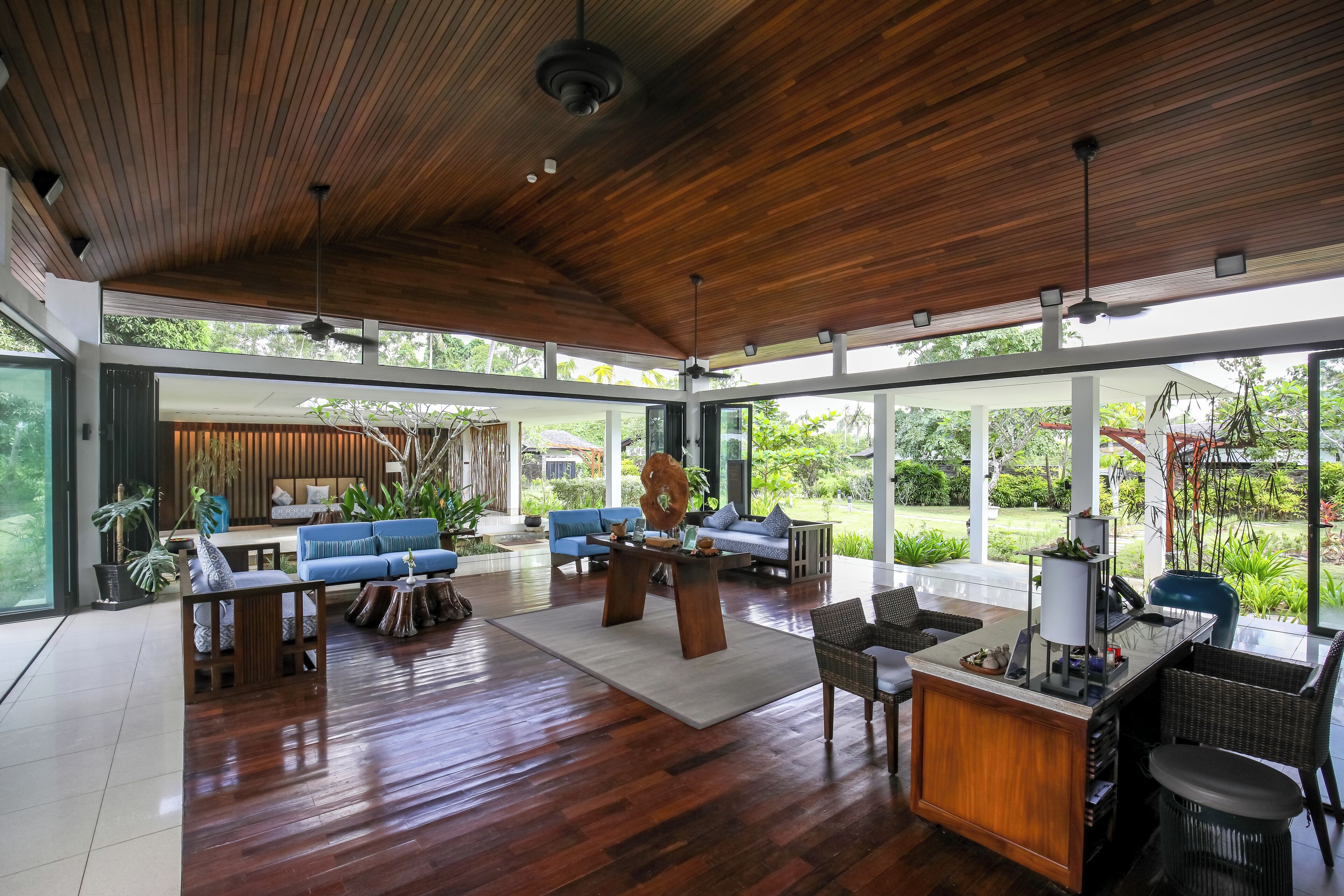 A spacious living area with a wooden ceiling, large windows, and a mix of seating arrangements including sofas and chairs.
