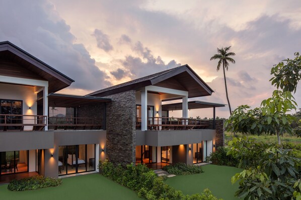 A modern two-story house with a balcony, large windows, and a well-maintained garden. - The Residence Bintan (Bintan)
