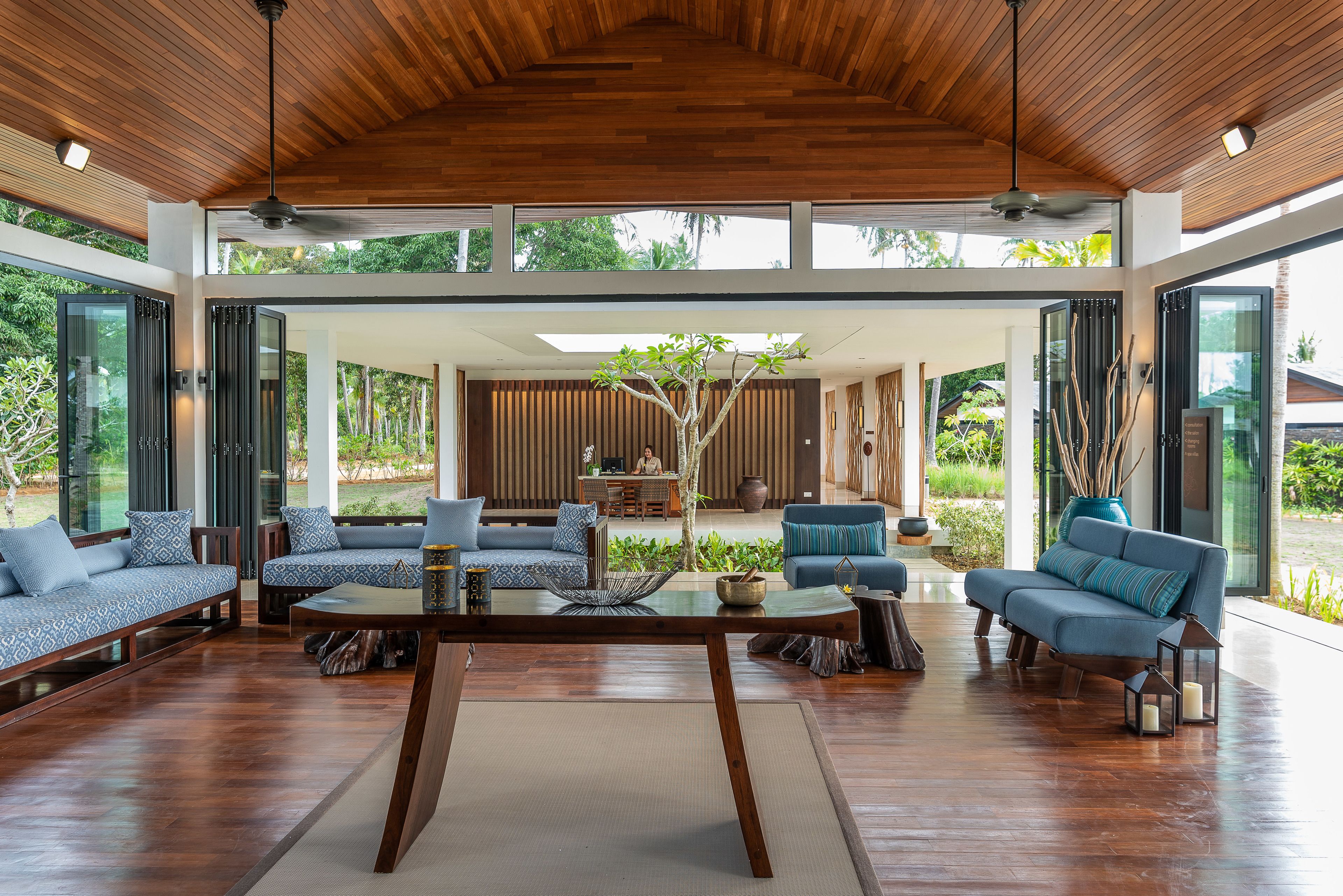 A spacious living area with a wooden ceiling, large windows, and a central seating arrangement.
