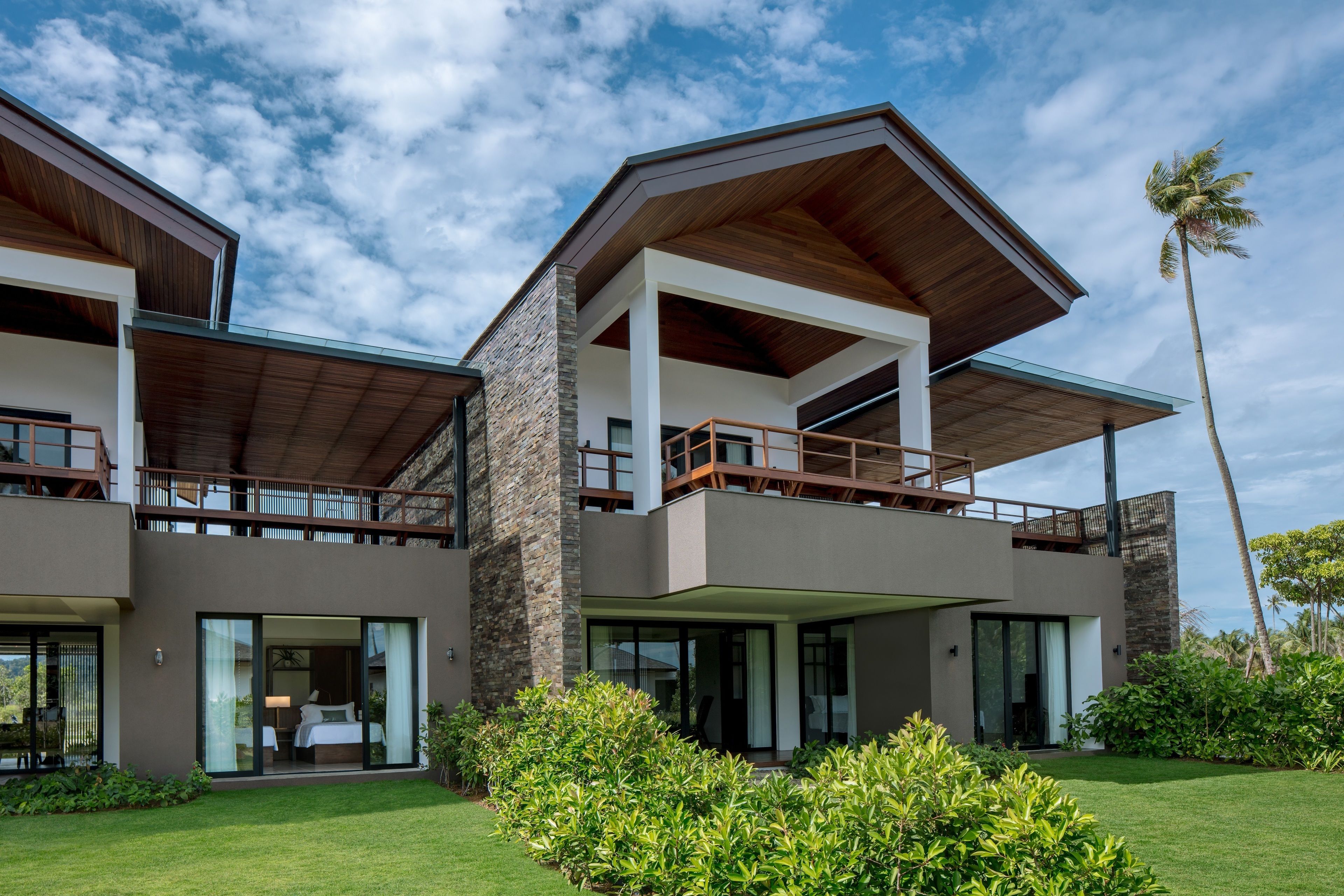 A modern two-story house with a balcony, large windows, and a well-maintained lawn.