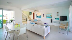 Una sala de estar moderna con un sofá blanco, una mesa de comedor con sillas, un televisor y obras de arte en las paredes.