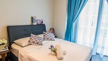 A bedroom with a large bed, a nightstand, a vase with flowers, and a window with blue curtains.