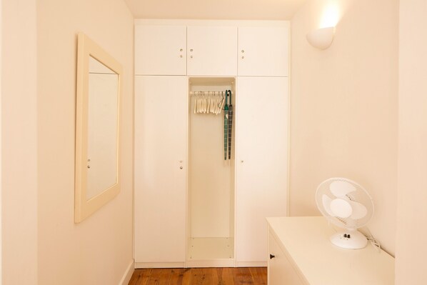 A room with a white wardrobe, a mirror, and a fan.
