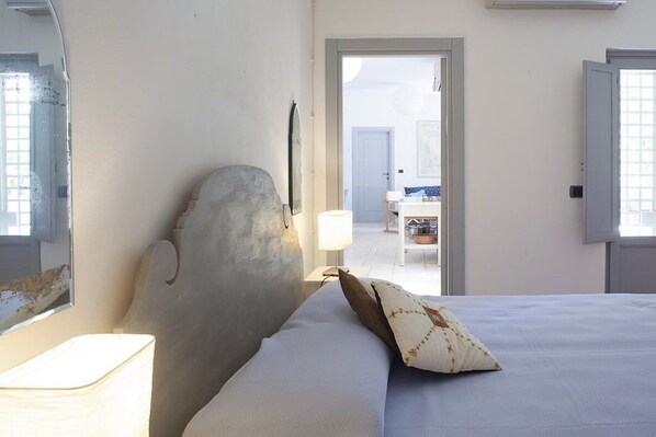 Une chambre à coucher avec un lit, une table de chevet, une lampe et une porte donnant sur une autre pièce.