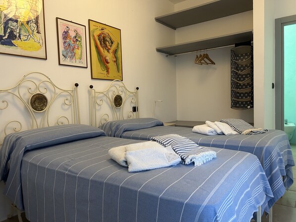A hotel room with two beds, each with striped bedding and towels. There are two framed artworks on the wall above the beds.