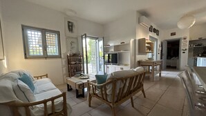Un salon spacieux comprenant un canapé, des fauteuils, une table à manger et un coin cuisine avec des placards et un téléviseur.