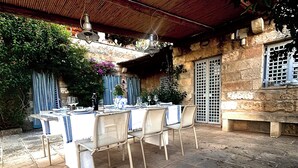 Un espace extérieur aménagé pour les repas, avec un sol en pierre, des nappes blanches et des chaises en métal.