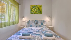 A neatly made bed with patterned bedding and two towels, a green curtain, and a painting on the wall. - Noelene - Cozy house, Private Pool, BBQ, Quiet area, Privacy (Valtura)