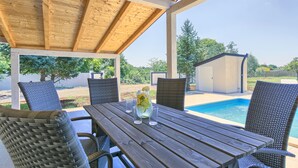 A covered patio with a pool, wicker chairs, and a table with a pitcher of lemonade. - Noelene - Cozy house, Private Pool, BBQ, Quiet area, Privacy (Valtura)