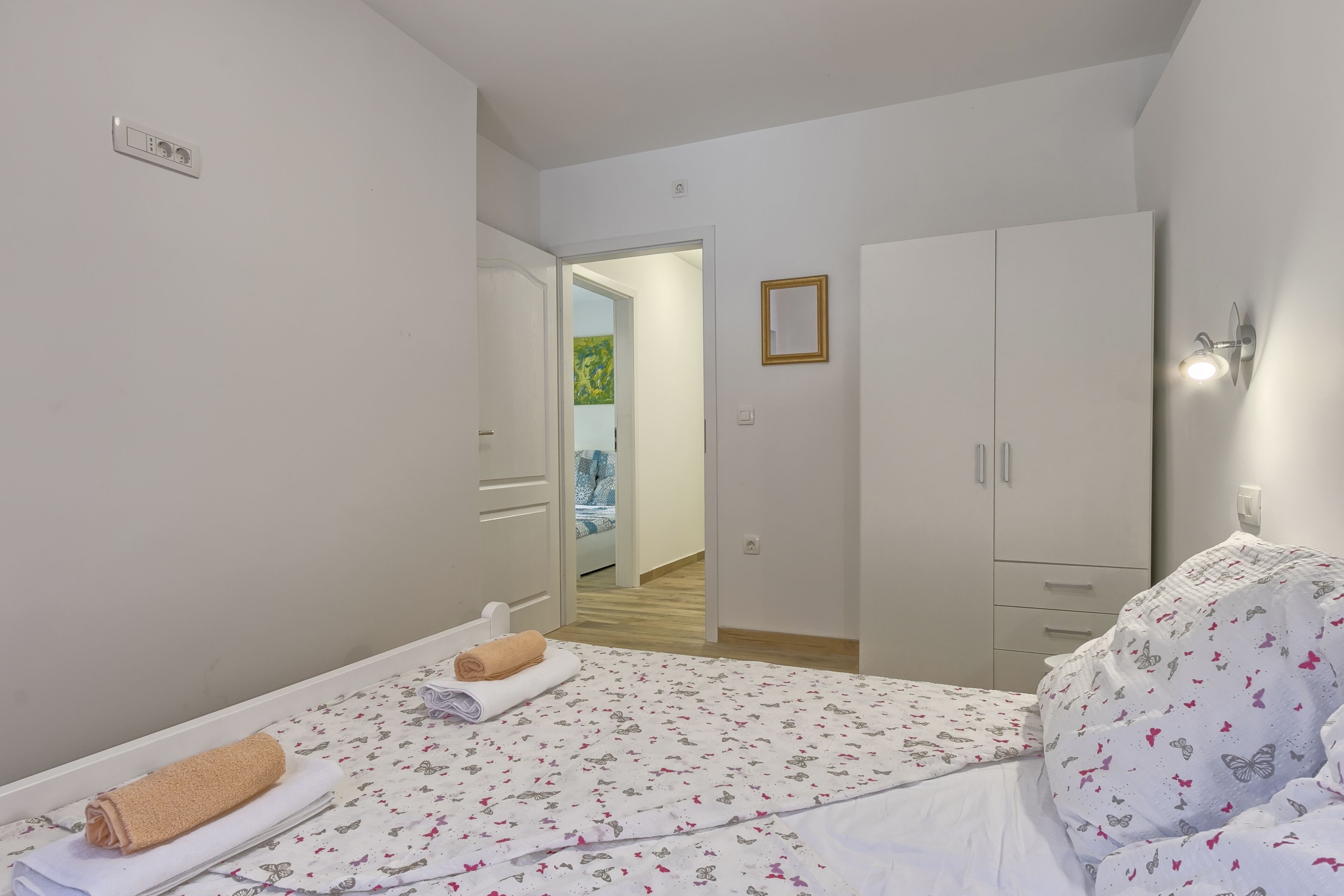 A bedroom with a bed, a wardrobe, a door leading to another room, and a wall-mounted light fixture.