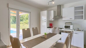 A modern kitchen with white cabinets, a dining table with chairs, a microwave, and a coffee maker. - Noelene - Cozy house, Private Pool, BBQ, Quiet area, Privacy (Valtura)