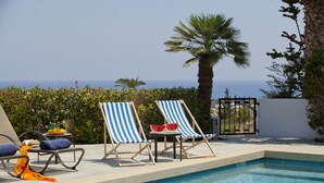 A poolside area with lounge chairs, a table with a watermelon, and a view of the ocean. - Protaras Pearl With Panoramic Sea View (Protaras)