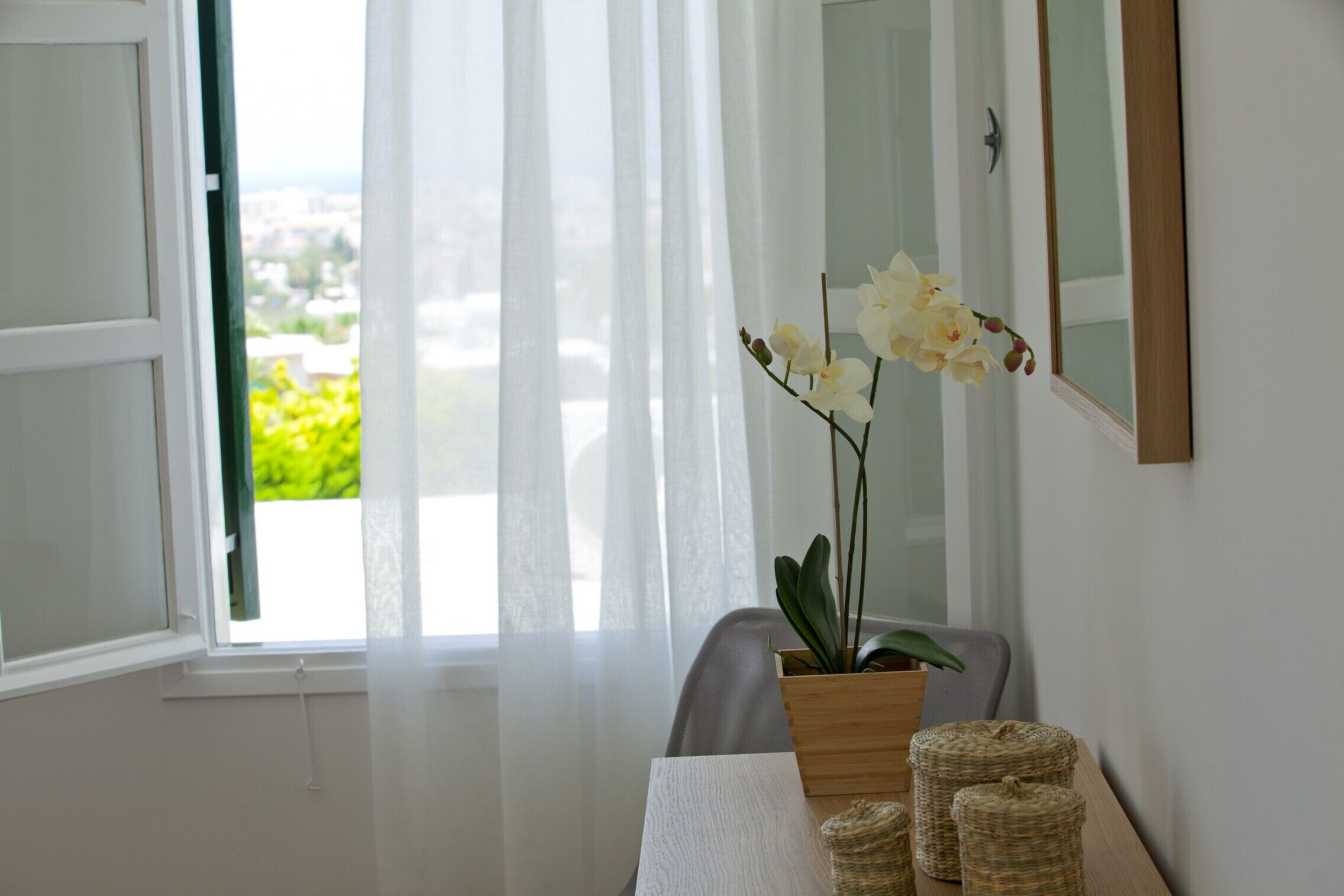 A room with a window, a potted orchid, wicker baskets, and a mirror on the wall.