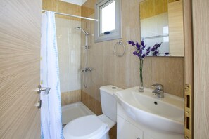 Et badeværelse med toilet, bruser, vask og spejl.