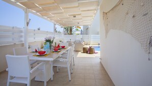 An outdoor dining area with white wicker chairs and a table set with a watermelon, flowers, and a vase. - Protaras Villa Posidonas 3 Near The Beach (Protaras)