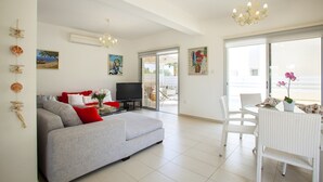 A spacious living room with a grey sofa, a flat-screen TV, and a dining area with white wicker furniture. - Protaras Villa Posidonas 3 Near The Beach (Protaras)