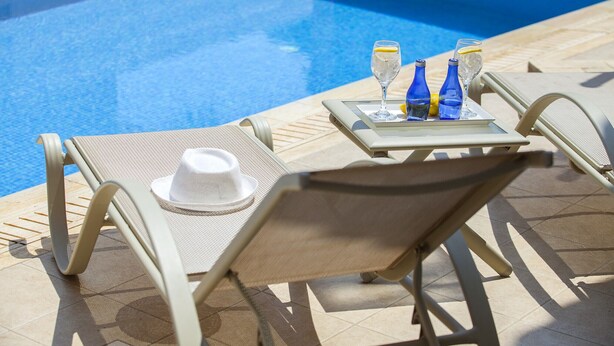 A poolside lounge area with sun loungers, a table with drinks, and a white hat. - Protaras Villa Posidonas 3 Near The Beach (Protaras)