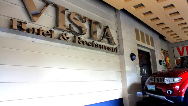 A hotel sign with the name "VISTA Hotel & Restaurant" and a red car parked in front.
