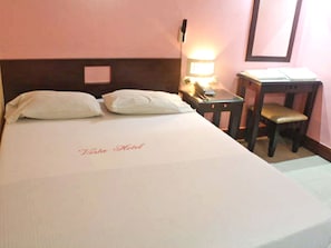 Quarto de hotel com cama, almofadas, mesa de cabeceira com abajur e uma cadeira.