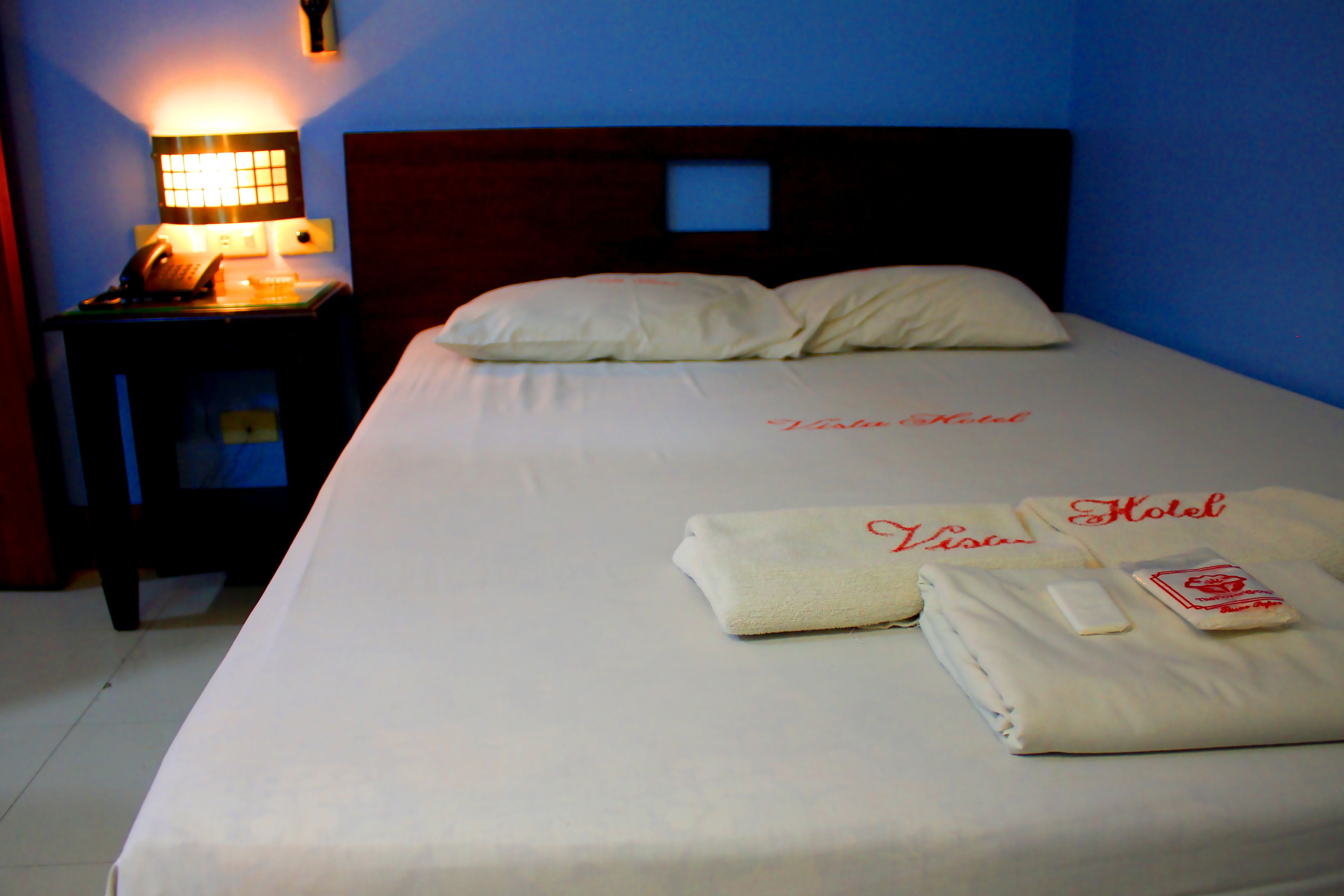A hotel room with a neatly made bed, a bedside table with a lamp, and a telephone.
