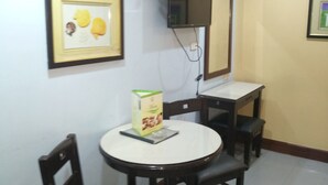Un comedor con una mesa redonda, cuatro sillas, un cuadro enmarcado en la pared, un televisor montado y un equipo de aire acondicionado.