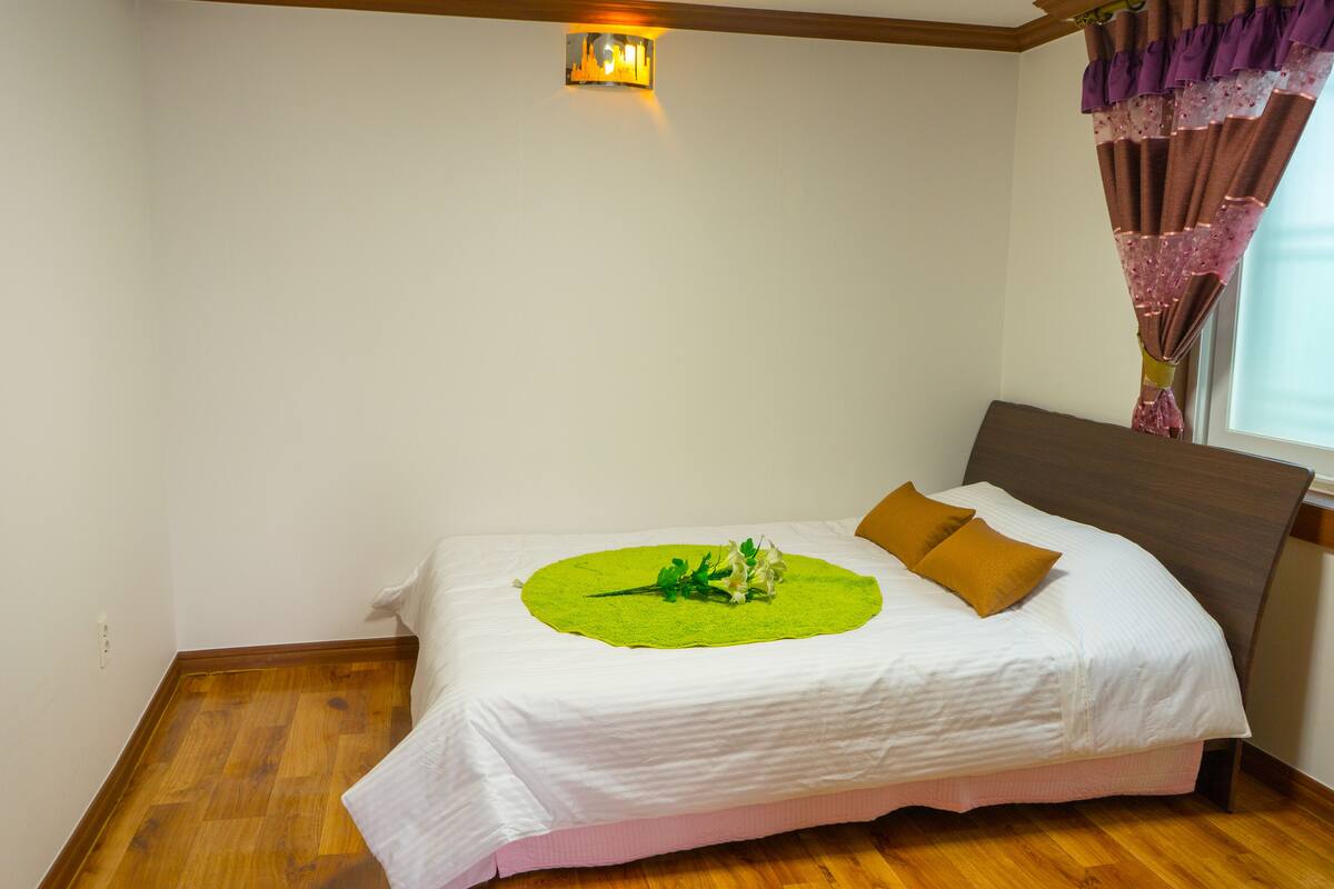 A neatly made bed with a green circular bedspread, two pillows, and a wooden headboard.