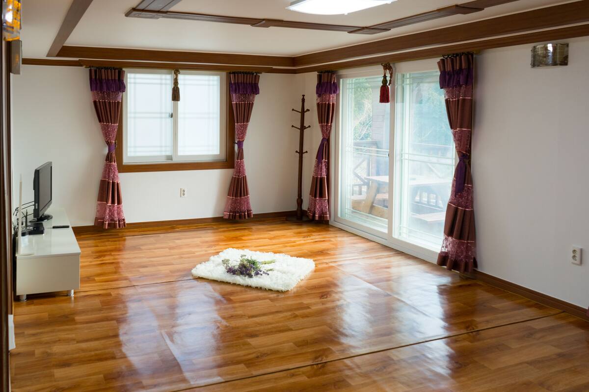 A room with wooden flooring, a white rug, and purple curtains.