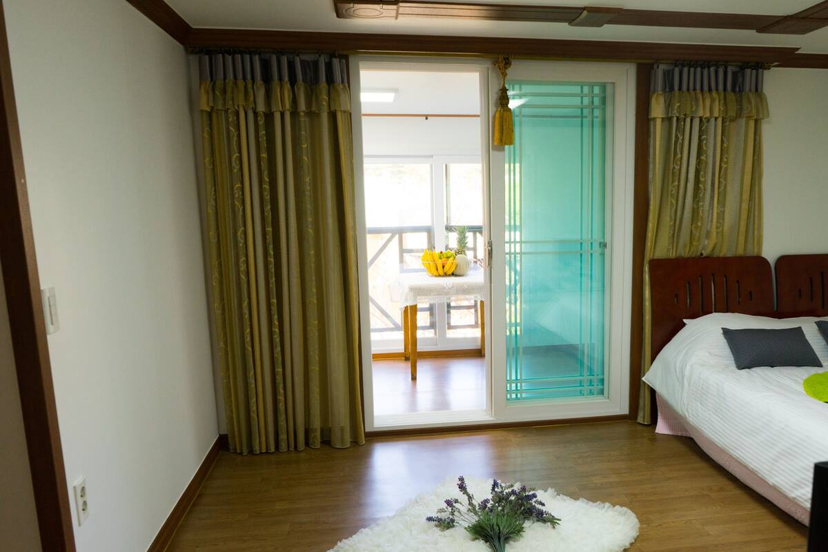 A bedroom with a bed, a white rug, and a view of a balcony with a table and chairs.