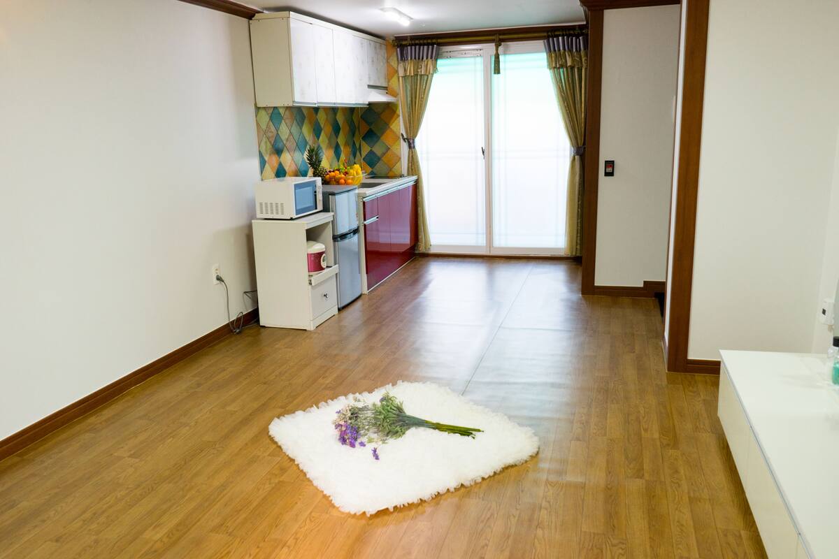 A kitchen with wooden flooring, a white rug with a bouquet of flowers, and a view of the outside through a sliding glass door.