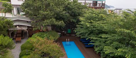 Un área de piscina con cubierta de madera, rodeada de abundante vegetación y un edificio con varios balcones.