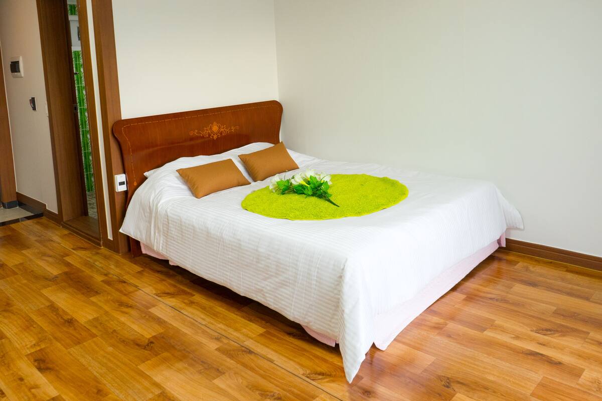 A neatly made bed with a white bedspread, two brown pillows, and a green floral arrangement on the bed.