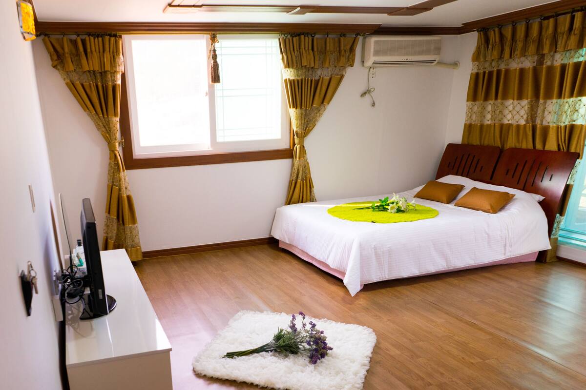 A bedroom with a bed, a desk, and a window with curtains.