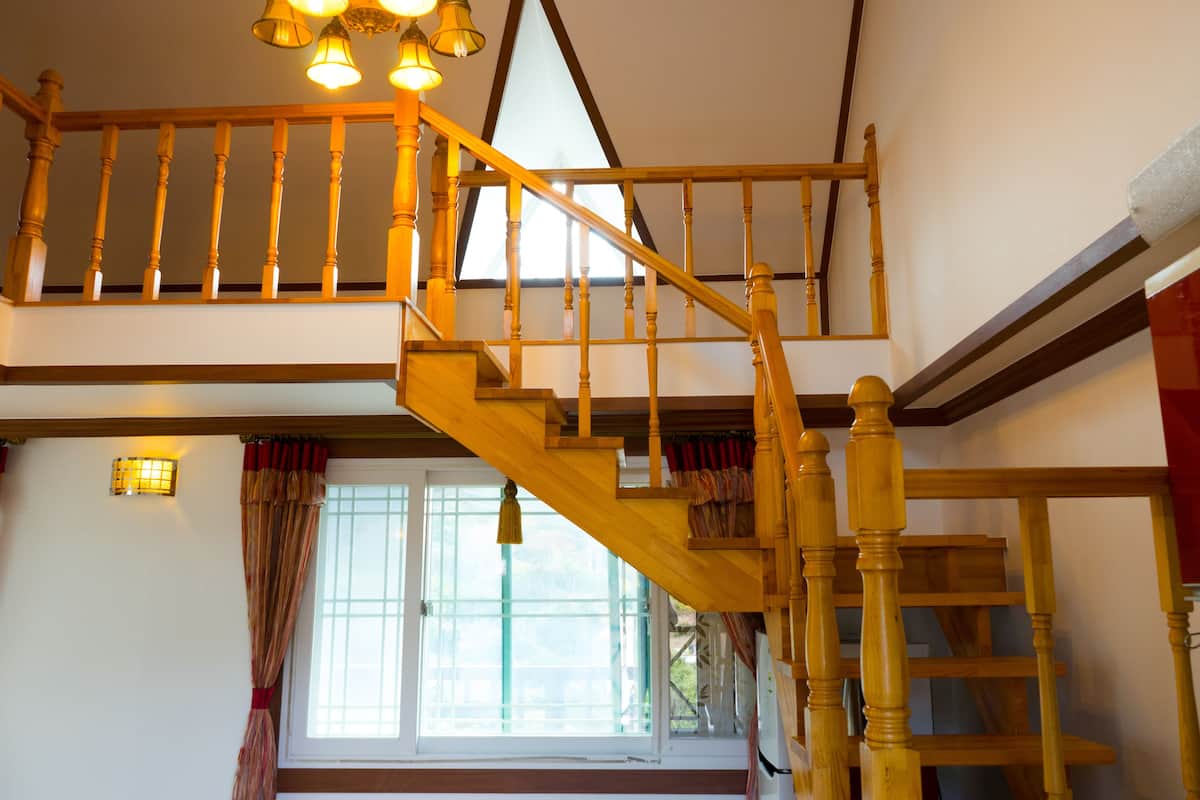 A wooden staircase with a handrail and a window with curtains.