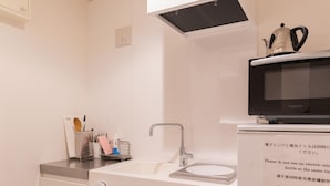 A modern kitchen with a white sink, stainless steel faucet, and a microwave oven. There is a kettle on top of the microwave, and a small shelf with kitchen utensils and a soap dispenser. - COCOSHUKU Tokyo Nakano (Tokyo)