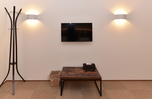 A room with a flat-screen TV mounted on the wall, a wooden table with a basket, a trash bin, and a floor lamp. - COCOSHUKU Tokyo Nakano (Tokyo)
