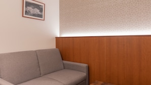 A neutral-toned sofa against a wooden panel wall, a framed picture on the wall, and a wooden table. - COCOSHUKU Tokyo Nakano (Tokyo)