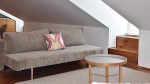 Een moderne loft slaapkamer met een grijze bank, een ronde houten tafel en een trap naar een hoger niveau.