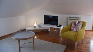 Een moderne woonkamer met een flatscreen televisie, een klein wit tafeltje, een gele fauteuil en een staande lamp.