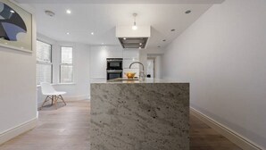 Una cocina moderna con una isla de mármol, horno empotrado y un amplio ventanal.